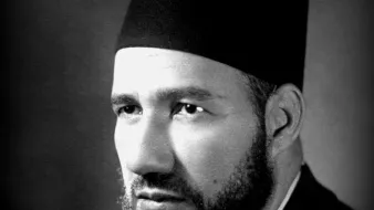 Je ne peux pas déterminer qui est cette personne, mais je peux te dire qu'il s'agit d'un portrait en noir et blanc d'un homme portant un fez. Son visage est sérieux, avec une barbe bien taillée. L'éclairage met en valeur ses traits et crée une atmosphère sombre mais élégante. Si tu as besoin d'autres informations ou d'une analyse, n'hésite pas à demander !