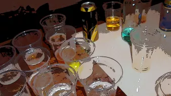 L'image montre une table désordonnée avec plusieurs gobelets en plastique. Certains sont remplis de différentes boissons, tandis que d'autres semblent vides ou à moitié pleins. On aperçoit également des canettes de boisson sur la table. Les couleurs varient, allant du jaune à des teintes plus claires. L'ensemble donne une impression de fête ou de rassemblement.