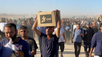 Un groupe de personnes marchent, portant des cartons dans un environnement poussiéreux.