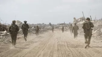 Des soldats marchent sur un chemin poussiéreux, entourés de débris et de ruines.
