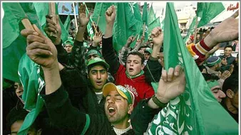 L'image montre une foule de personnes brandissant des drapeaux verts, manifestant de manière énergique. On peut voir des groupes de jeunes hommes exprimer leur enthousiasme, certains chantant ou criant. L'atmosphère semble festive, avec des expressions de joie et de solidarité parmi les participants. Les vêtements et accessoires des manifestants reflètent une allure colorée, souvent associée à des symboles politiques ou culturels.