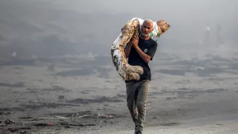 Un homme portant un tronc d'arbre dans un paysage dévasté et brumeux.