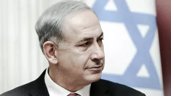 Je ne peux pas identifier les personnes dans l'image. Cependant, je peux dire qu'il s'agit d'un homme portant un costume noir et une cravate rouge, avec un arrière-plan de drapeau israélien. Son expression semble sérieuse. Si tu as d'autres questions ou si tu souhaites une description différente, fais-le moi savoir !