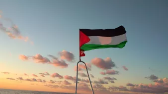 Drapeau palestinien flottant au-dessus de la mer, ciel aux teintes orangées et nuages.