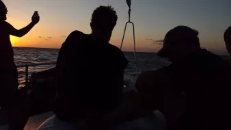 Silhouettes de personnes sur un bateau au coucher du soleil, mer calme.