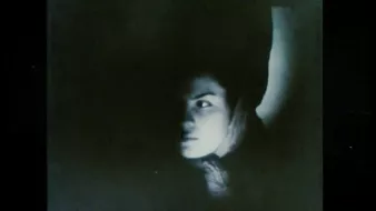 L'image présente un contraste marquant entre ombre et lumière, mettant en avant le visage d'une personne. Son expression semble intrigante, avec un regard perçant qui capte l'attention. On distingue également un bras, suggérant une posture dynamique. L'ambiance générale est mystérieuse et un peu sombre, ce qui peut susciter diverses interprétations émotionnelles.