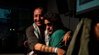 Deux hommes s'étreignent, souriants, avec des déguisements et un ambiance chaleureuse.