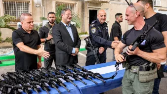 Des hommes en uniforme échangent des armes sur une table, sourires et discussions.