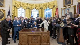 Groupe d'hommes et femmes autour d'un bureau, avec une personne signant un document.