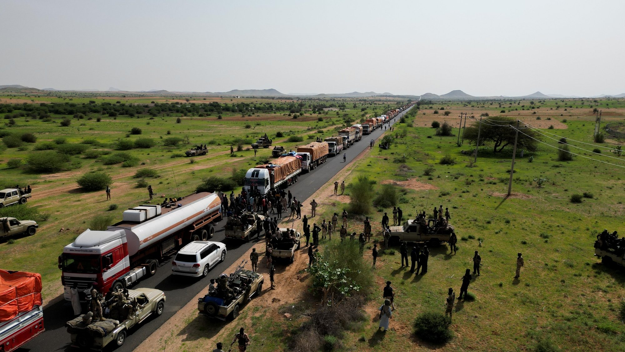 Una lunga fila di veicoli su una strada in un paesaggio verde e desertico.