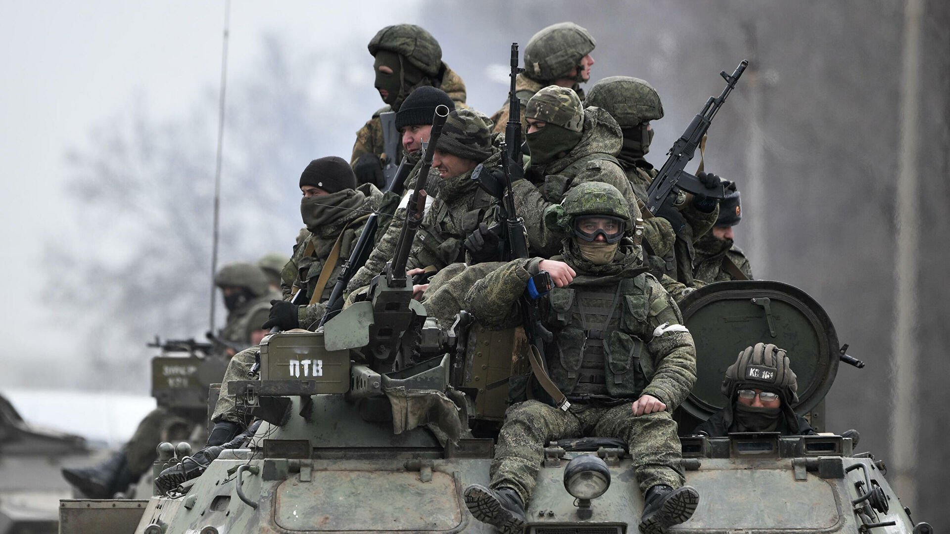L'immagine mostra un gruppo di soldati equipaggiati con abbigliamento militare e armi, che si trovano su un veicolo blindato. Alcuni di loro indossano maschere o occhiali protettivi, mentre altri appaiono attenti e pronti all'azione. Il contesto è probabilmente un'area di conflitto, con un paesaggio grigio e invernale sullo sfondo. L'atmosfera è seria e tesa, riflettendo la situazione militare.