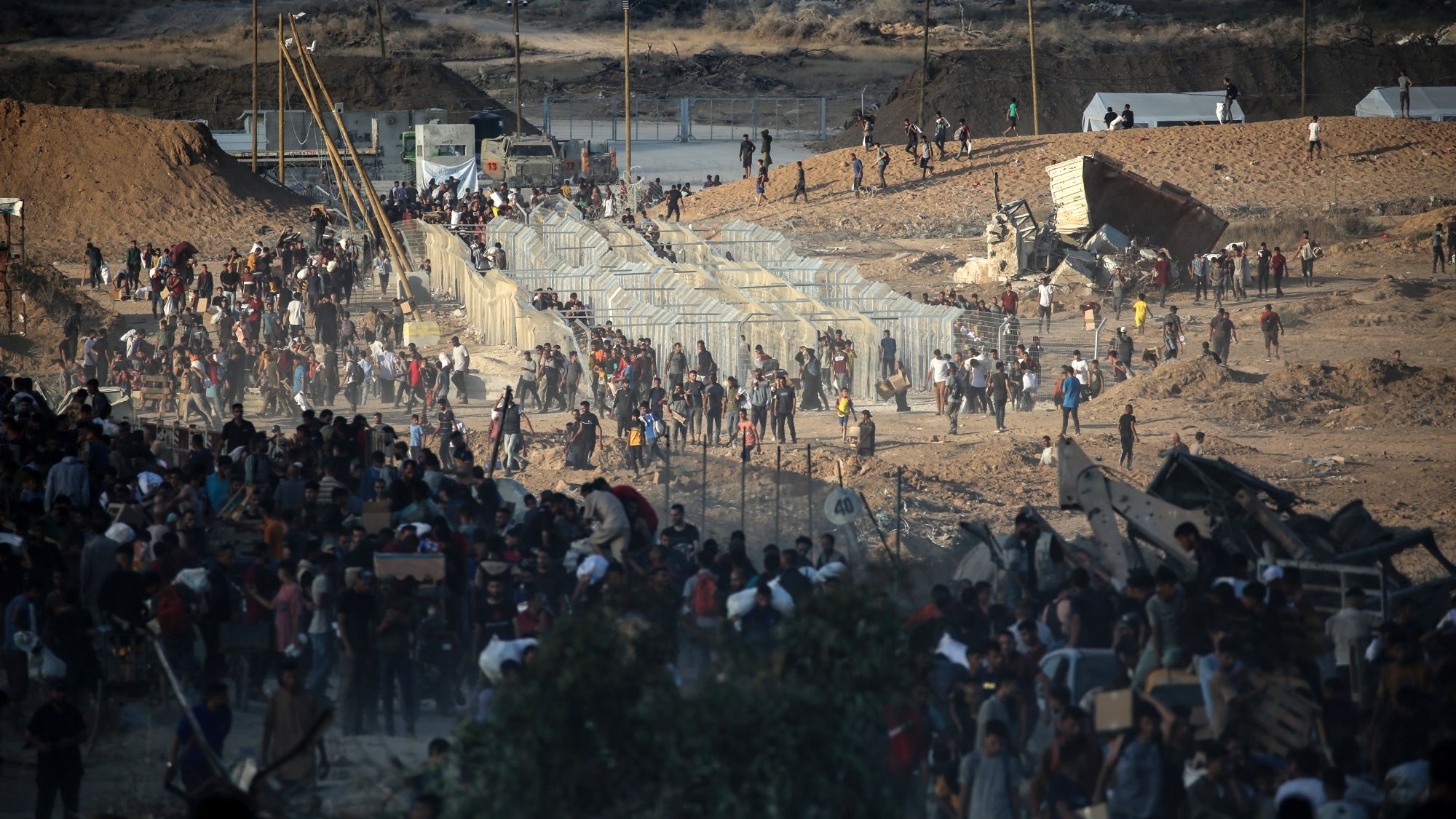 Persone in movimento vicino a barriere in un paesaggio arido e affollato.