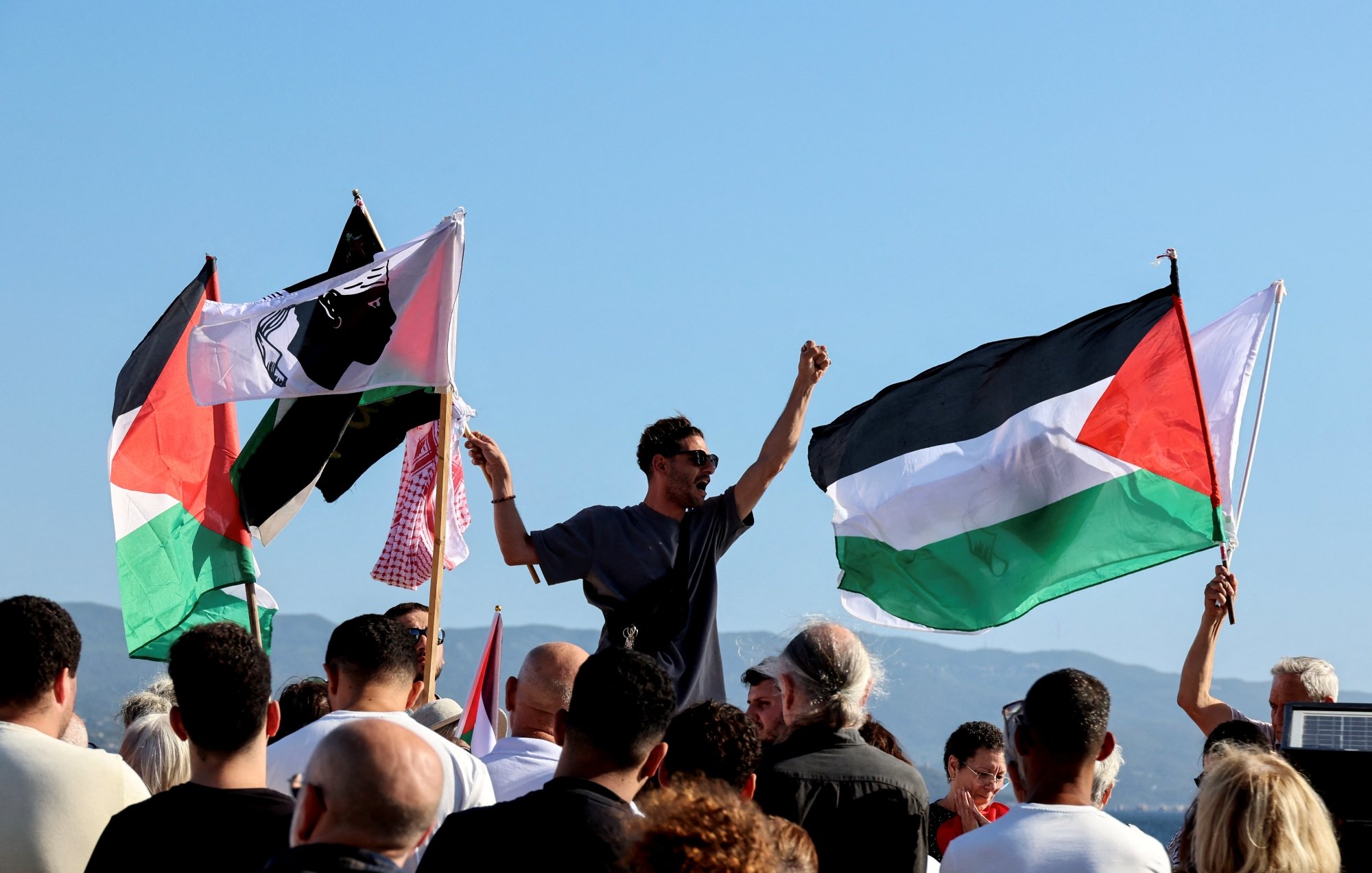 Manifestazione con persone che sventolano bandiere palestinesi e gridano slogan.