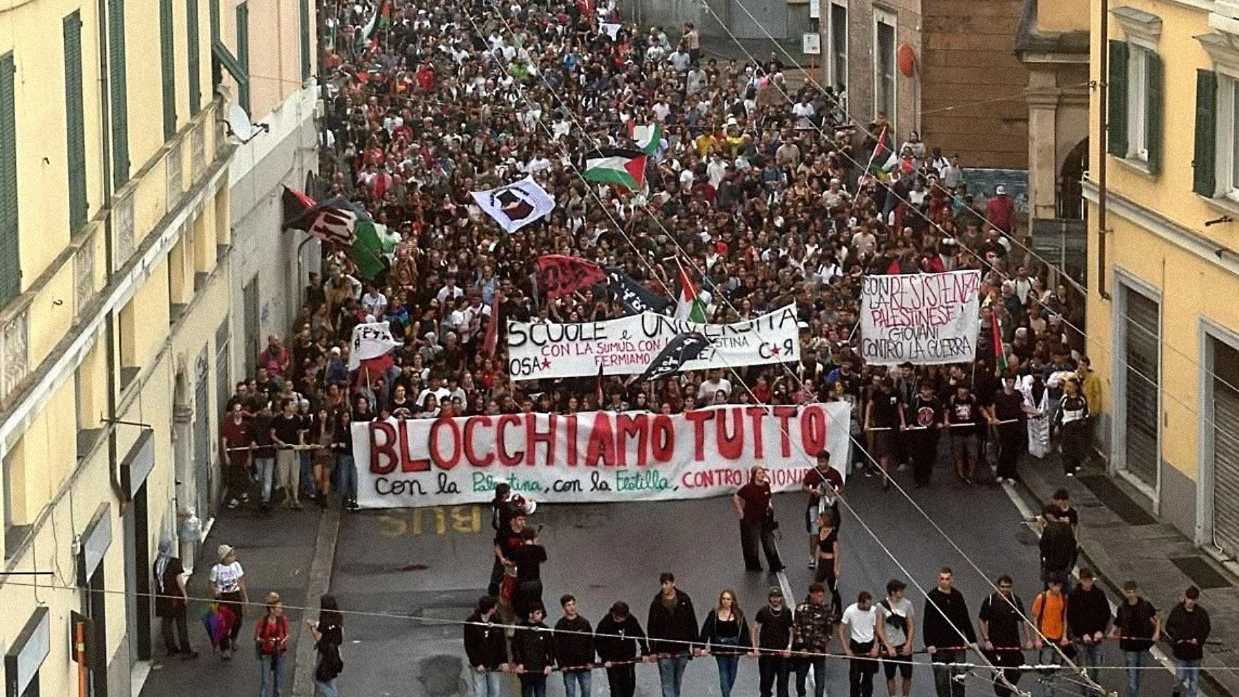 Una grande manifestazione con moltissime persone che sfilano, portando striscioni.