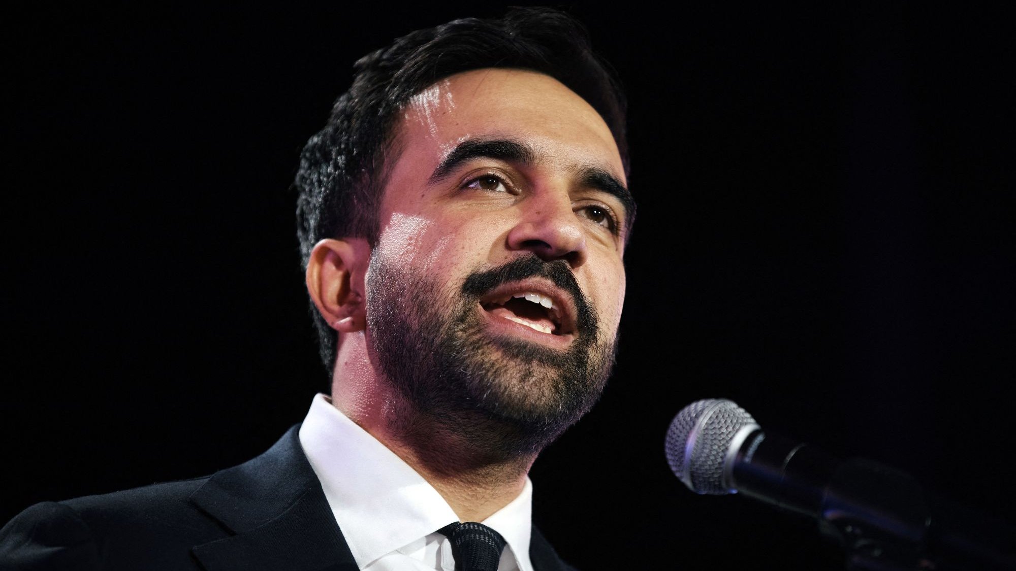 Uomo in giacca scura parla al microfono, esprime passione e coinvolgimento.