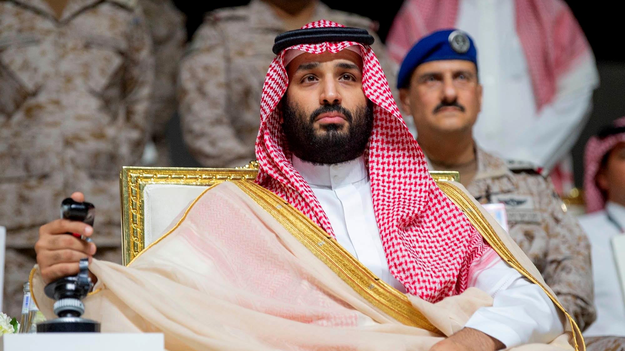 Un uomo in abiti tradizionali arabi, seduto su una sedia dorata, con uno sguardo serio.