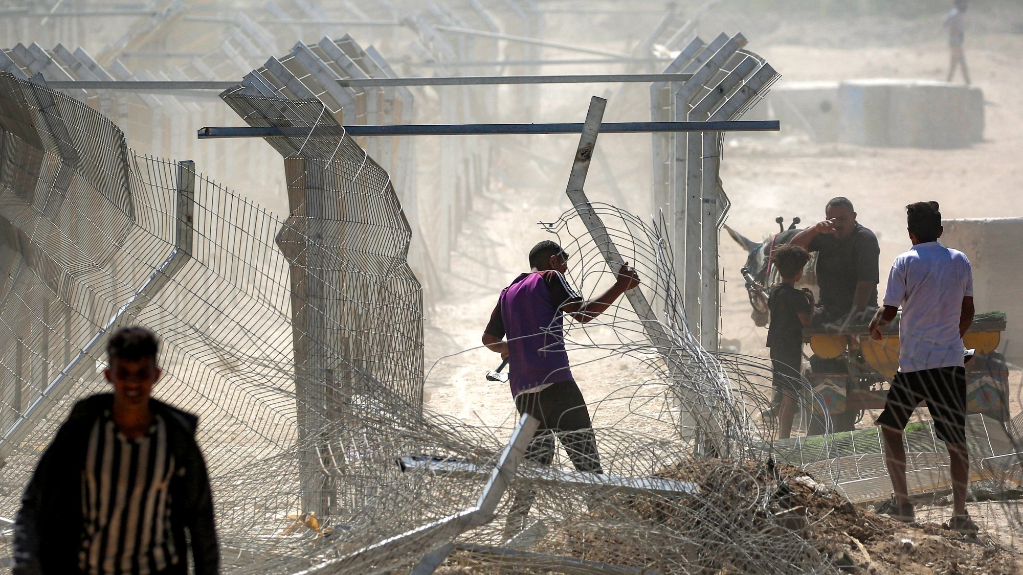 Uomini vicino a una recinzione di filo spinato in un'area polverosa e confusa.
