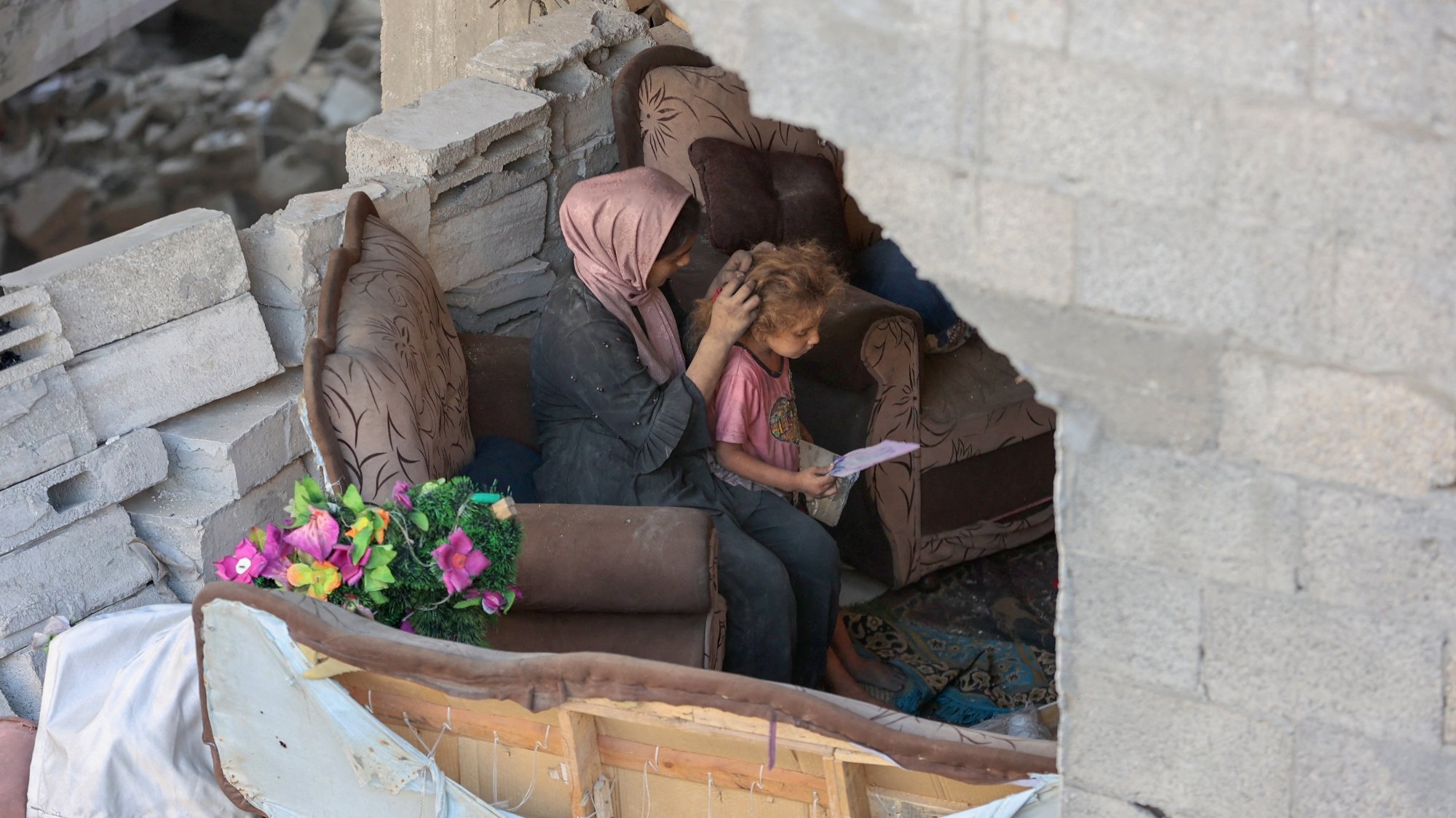 Due persone sedute su un divano in un ambiente distrutto, circondate da macerie.