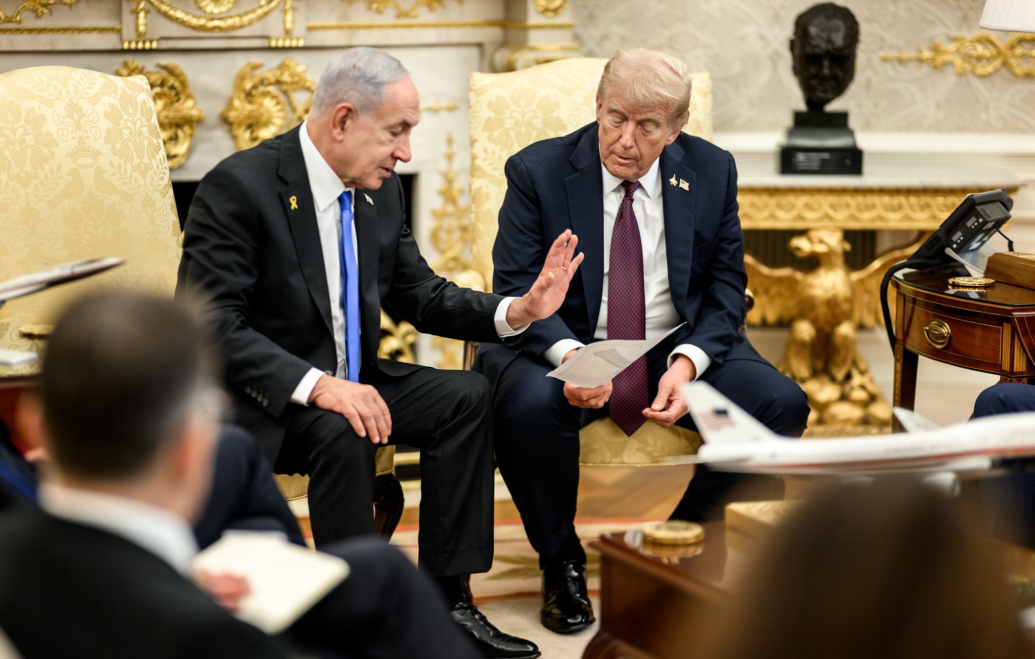 Due uomini in abiti formali discutono seduti su poltrone in un ambiente elegante.