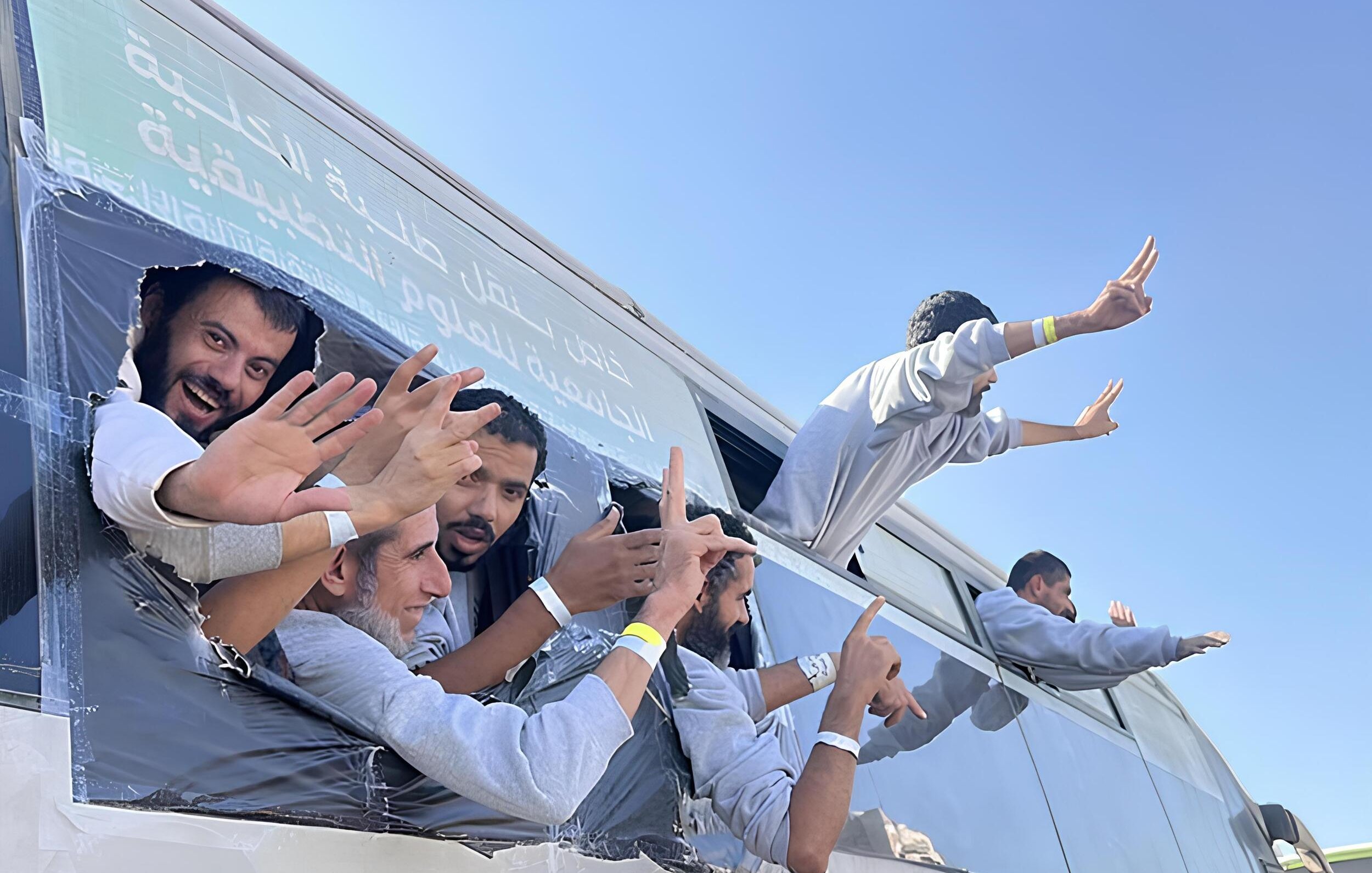 Gruppo di persone sorridenti sporge da un bus con le mani alzate, in un'atmosfera festosa.
