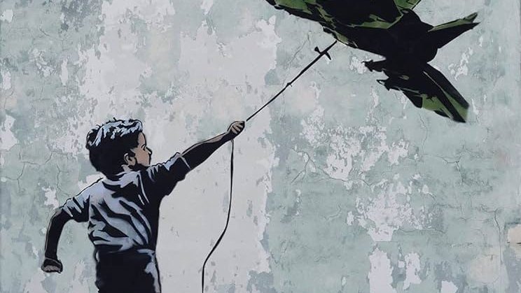 L'immagine rappresenta un bambino che corre e tiene in mano un filo da cui pende un aereo da guerra in miniatura. Il bambino sembra gioioso, mentre lo sfondo è costituito da un muro scrostato con tonalità chiare e imperfezioni visibili. L'aereo, di colore verde militare, contrasta con l'innocenza del bambino e il suo gesto, creando una riflessione evocativa sul tema della guerra e della gioventù.