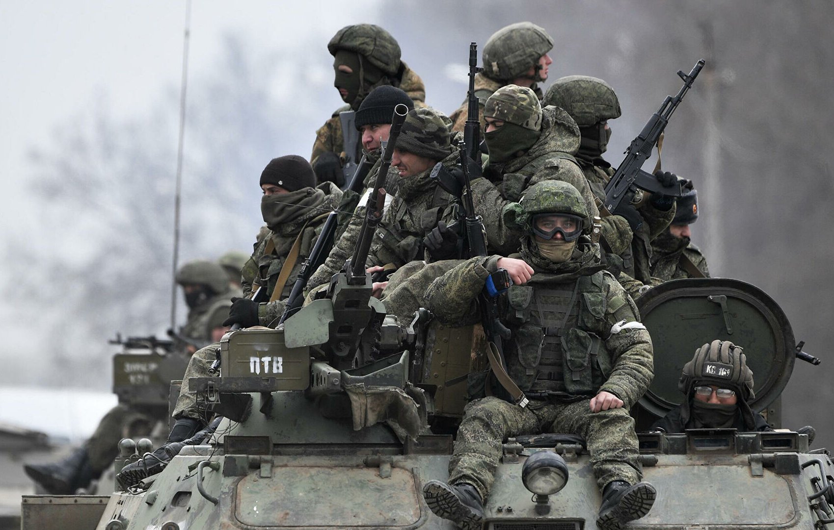 L'immagine mostra un gruppo di soldati equipaggiati con abbigliamento militare e armi, che si trovano su un veicolo blindato. Alcuni di loro indossano maschere o occhiali protettivi, mentre altri appaiono attenti e pronti all'azione. Il contesto è probabilmente un'area di conflitto, con un paesaggio grigio e invernale sullo sfondo. L'atmosfera è seria e tesa, riflettendo la situazione militare.