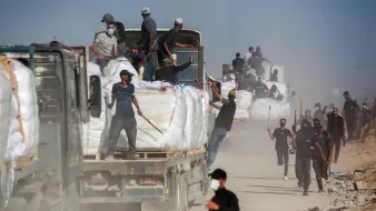 Un gruppo di persone lavora attorno a camion in una zona polverosa.