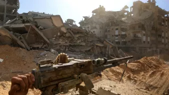 Una zona devastata, edifici crollati e un fucile appoggiato su un treppiede.