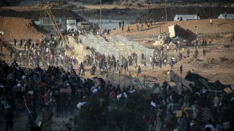 Persone in movimento vicino a barriere in un paesaggio arido e affollato.