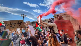 Una manifestazione colorata con fumogeni rossi e cartelli per la Palestina.