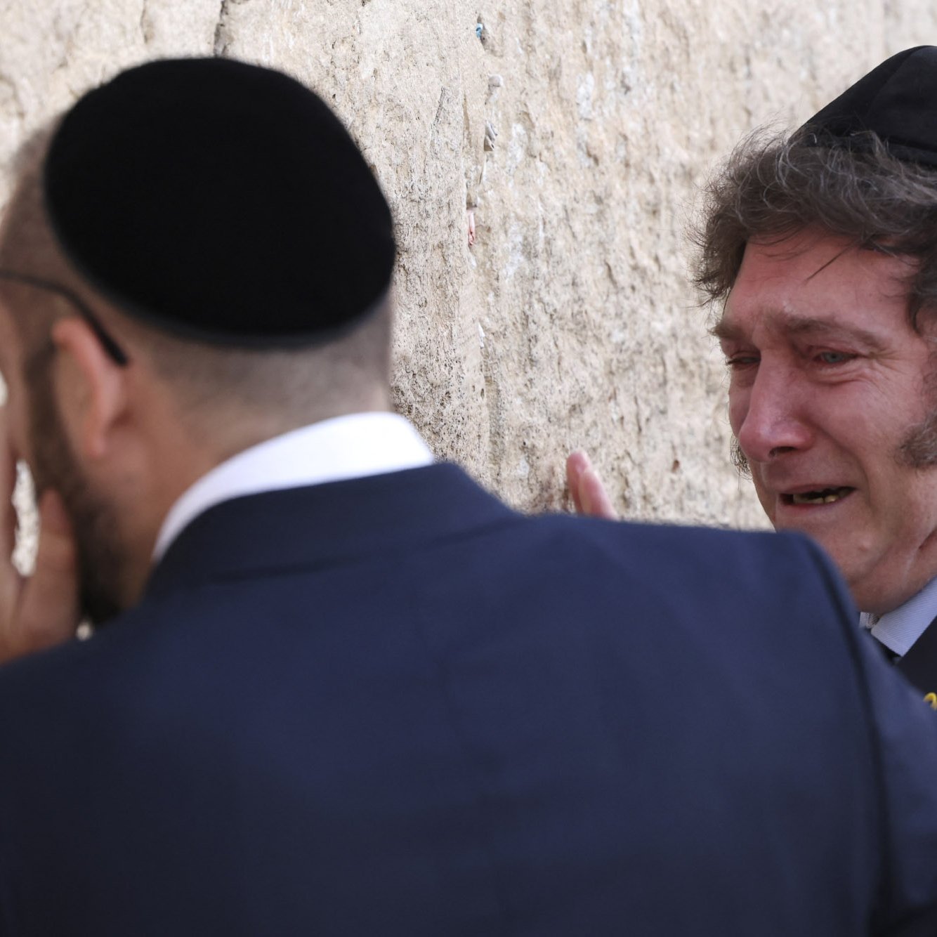 در این تصویر، دو مرد یهودی را مشاهده می‌کنیم که در کنار دیواری ایستاده‌اند. یکی از آنها در حال گریه کردن است و احساسات عمیقی را نشان می‌دهد. هر دو مرد کلاه یهودی (کیپا) بر سر دارند و در حال ادای احترام یا دعا به دیوار هستند. دیوار ممکن است دیوار گریه باشد که برای یهودیان مقدس است. پس‌زمینه تصویر با سنگ‌های بی شکل و طبیعی پر شده است.