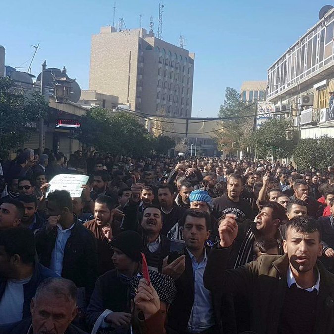The image depicts a large crowd of people gathered on a street, likely participating in a protest or demonstration. The individuals appear to be expressing their views passionately, with some holding signs. The setting includes buildings and urban infrastructure, indicating the event is taking place in a city. The atmosphere seems intense, with many people visible in the foreground and background, suggesting a significant turnout for the event.