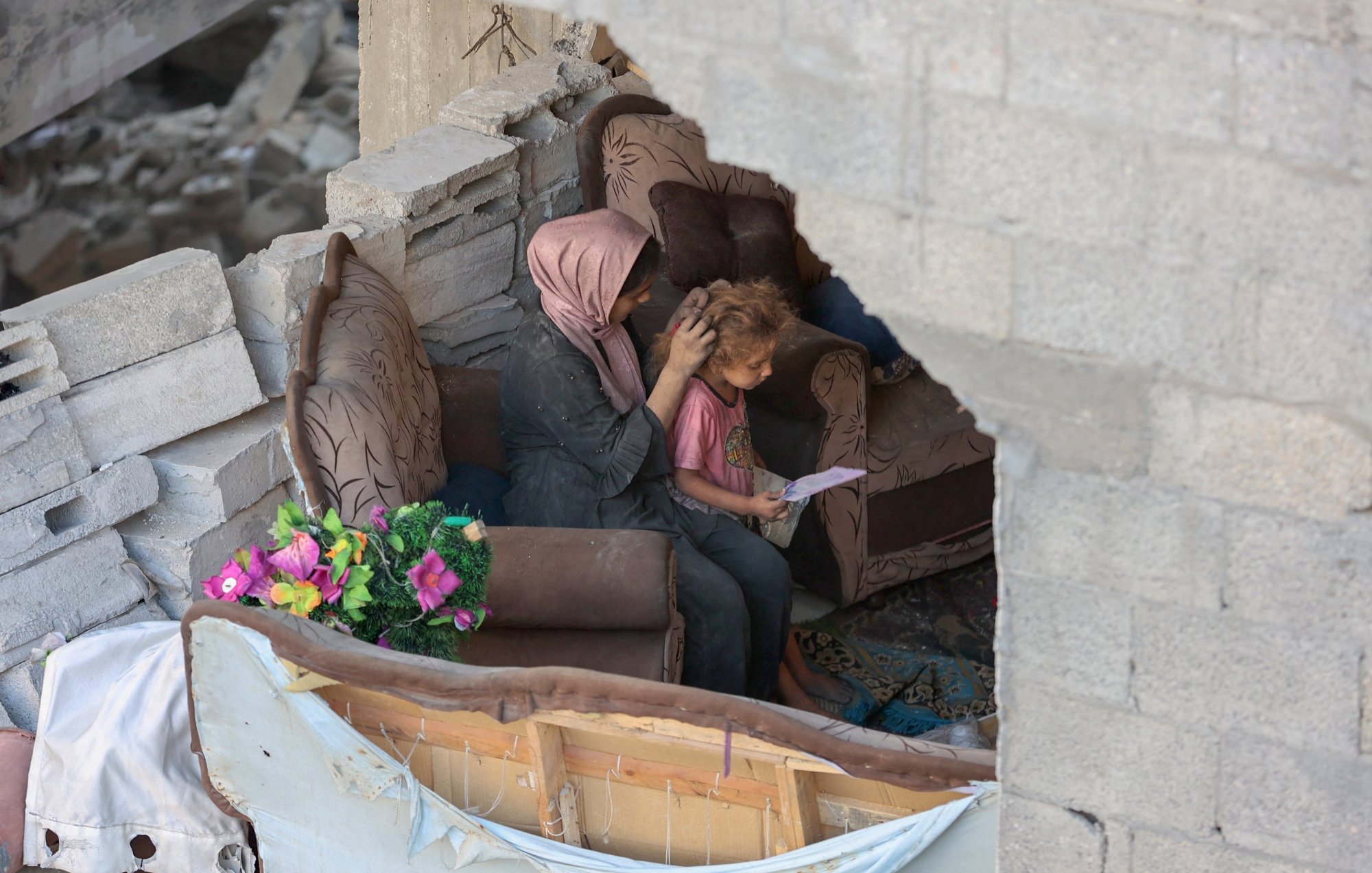Due persone sedute su un divano in un ambiente distrutto, circondate da macerie.