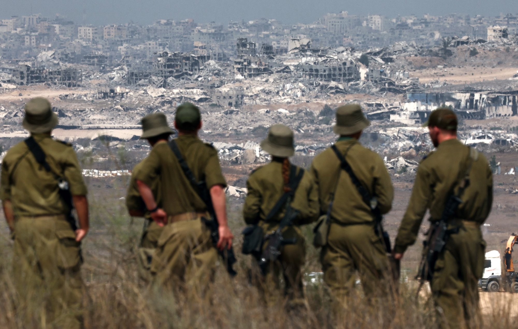 Des soldats en uniforme observant des ruines de bâtiments en arrière-plan.
