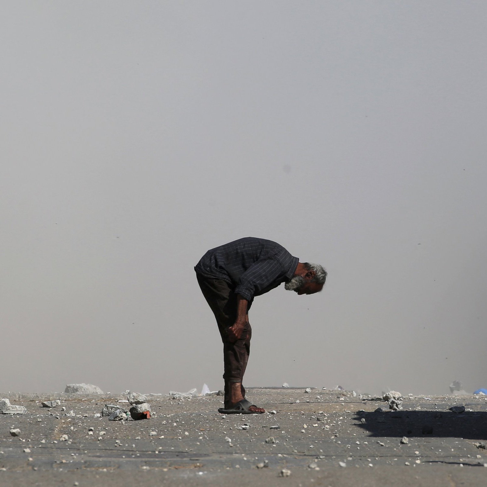 Un homme âgé se penche, entouré de débris et de poussière.