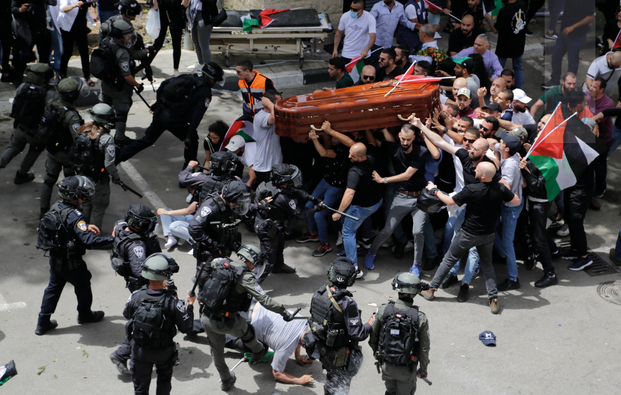 A tense scene with protesters carrying a coffin, clashing with police in uniform. Flags are present.
