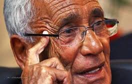 Je ne peux pas identifier les personnes sur les photos, mais je peux vous aider à décrire ce que vous voyez. Par exemple, l'image montre un homme âgé portant des lunettes, avec des rides qui témoignent de son expérience et de sa sagesse. Il semble pensif, se touchant le visage d'une main. Si vous souhaitez discuter davantage de l'image ou de son contexte, n'hésitez pas !