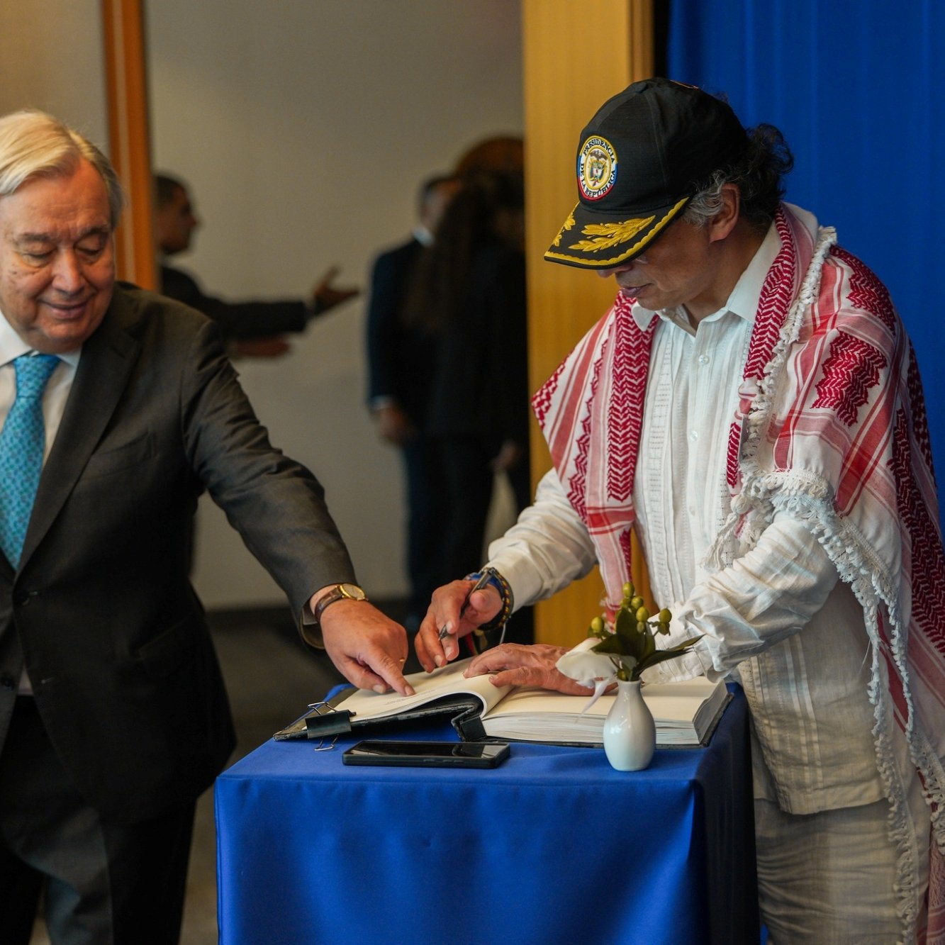 Deux hommes, l'un en costume et l'autre en tenue traditionnelle, signent un livre ensemble.