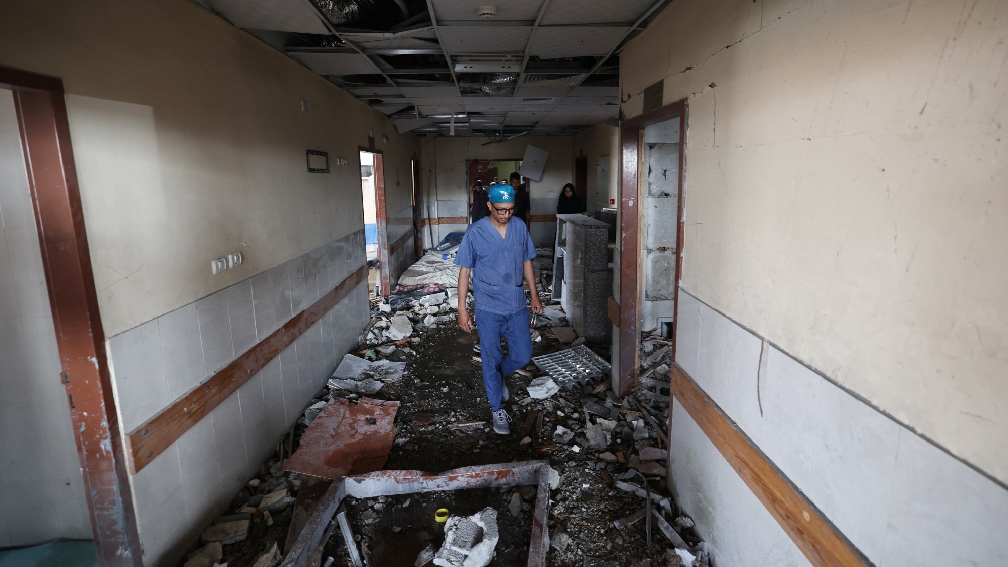 Couloir d'un bâtiment endommagé, débris partout, homme en tenue de protection avance prudemment.