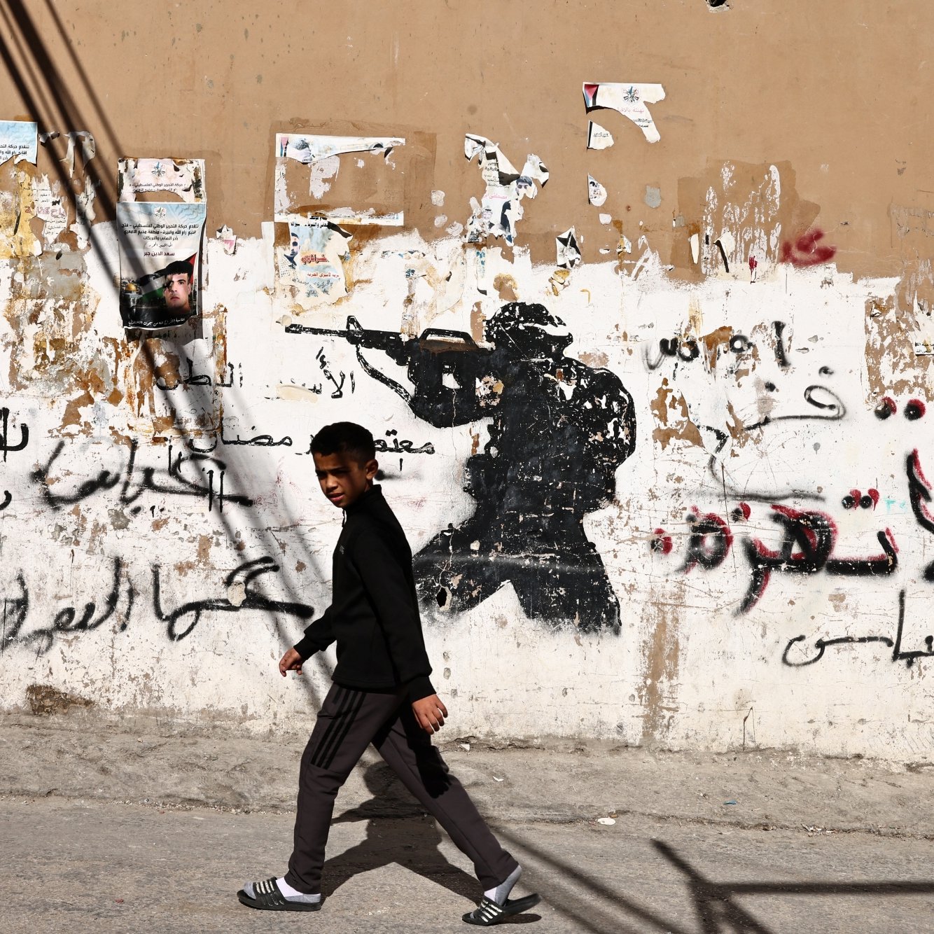 Un garçon marche devant un mur graffiti avec une silhouette de soldat.