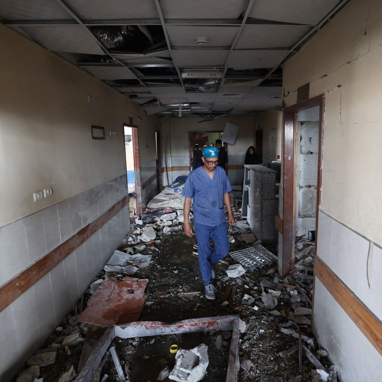 Couloir d'un bâtiment endommagé, débris partout, homme en tenue de protection avance prudemment.
