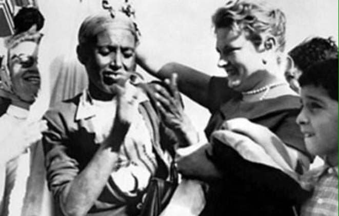 این تصویر یک صحنه اجتماعی و شاداب را نشان می‌دهد. در مرکز تصویر، یک زن و یک مرد در حال شادی و گفت‌وگو هستند. مرد ظاهراً لباس محلی یا سنتی پوشیده است و به نظر می‌رسد در حال رقصیدن یا آهنگ زدن است. زن دیگری که در کنار مرد ایستاده، لبخند می‌زند و به نظر می‌رسد از صحنه لذت می‌برد. همچنین چند نفر دیگر در زمینه تصویر دیده می‌شوند که به این شادی افزوده‌اند. فضای کلی تصویر به حس دوستی و جشن نزدیک است.