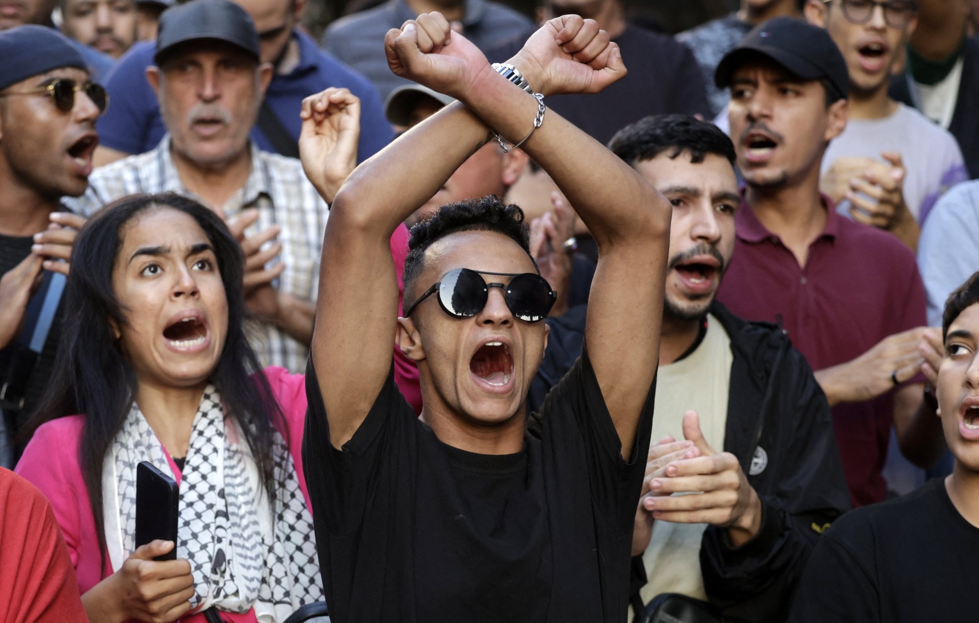 Groupe de manifestants exprimant des émotions fortes, certains brandissant les bras.