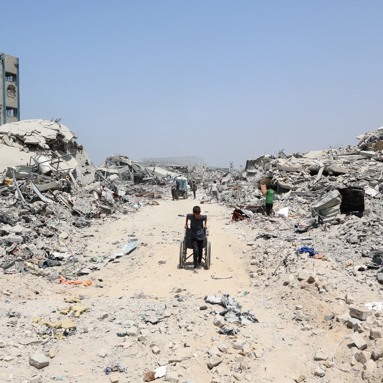 Un chemin au milieu des ruines, une personne en fauteuil roulant avance lentement.