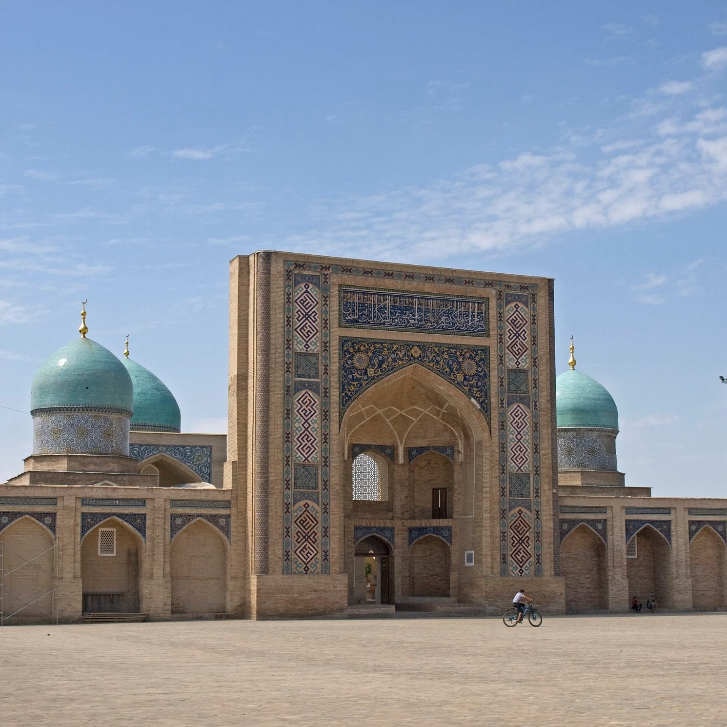 تظهر الصورة معمارًا تاريخيًا بأقواس وقباب زرقاء في سماء صافية. جو مريح.