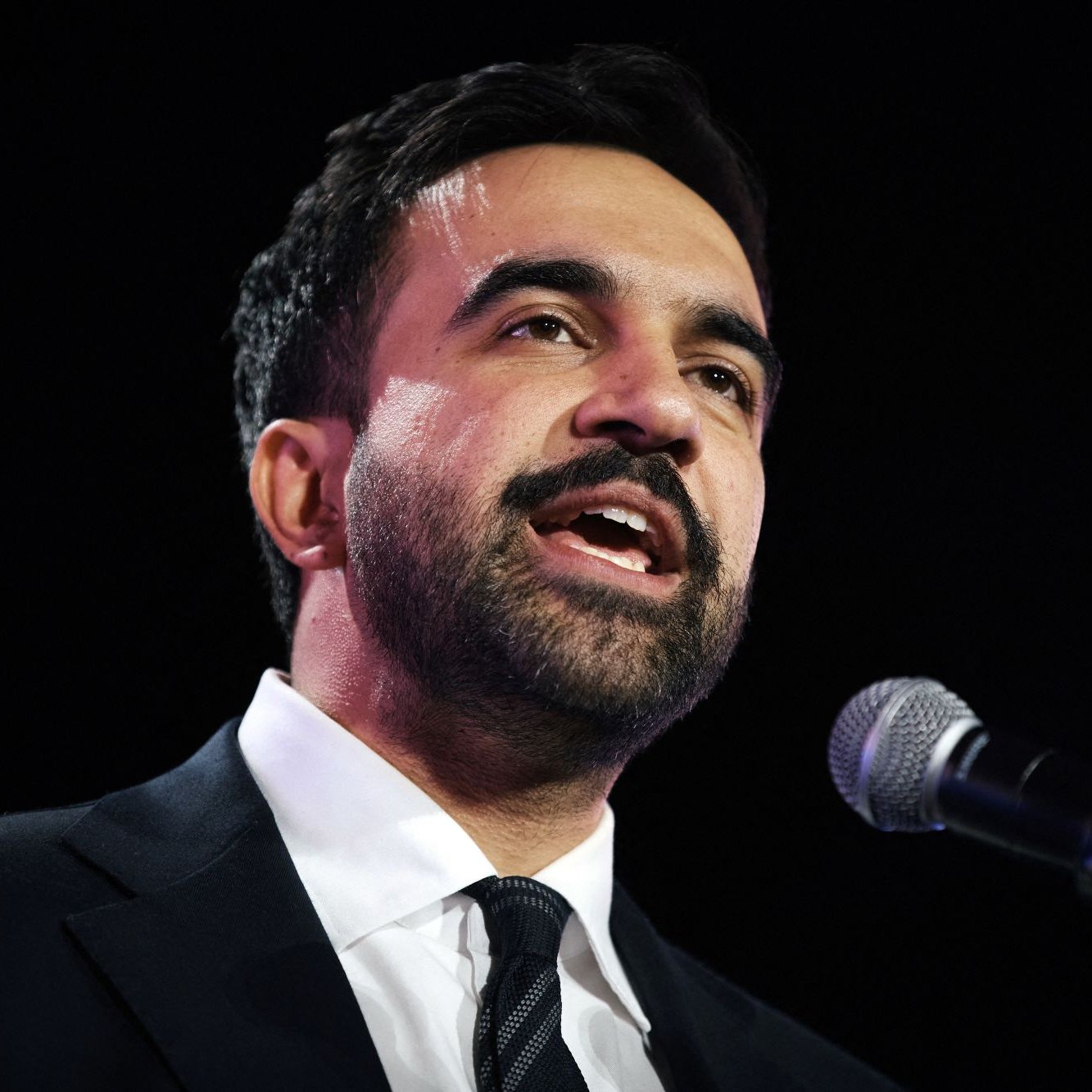 Uomo in giacca scura parla al microfono, esprime passione e coinvolgimento.