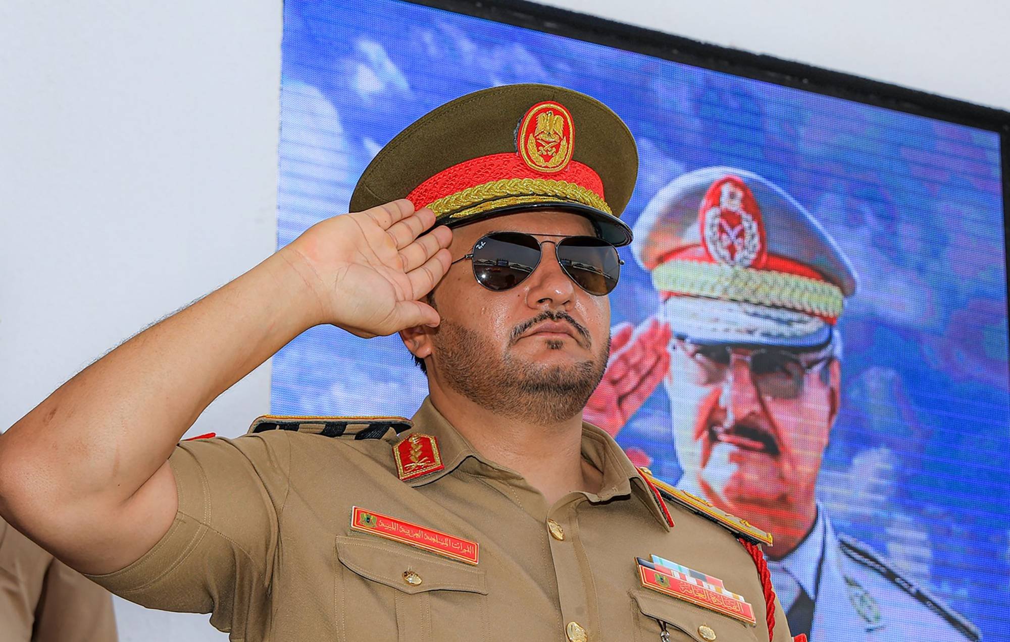 ضابط عسكري يرتدي زيًا رسميًا ونظارات شمسية، يؤدي تحية عسكرية.