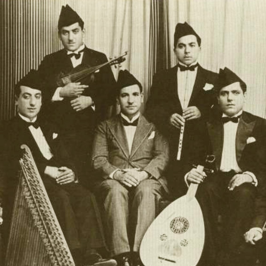Groupe de musiciens en costume noir, instruments variés, ambiance d'époque.