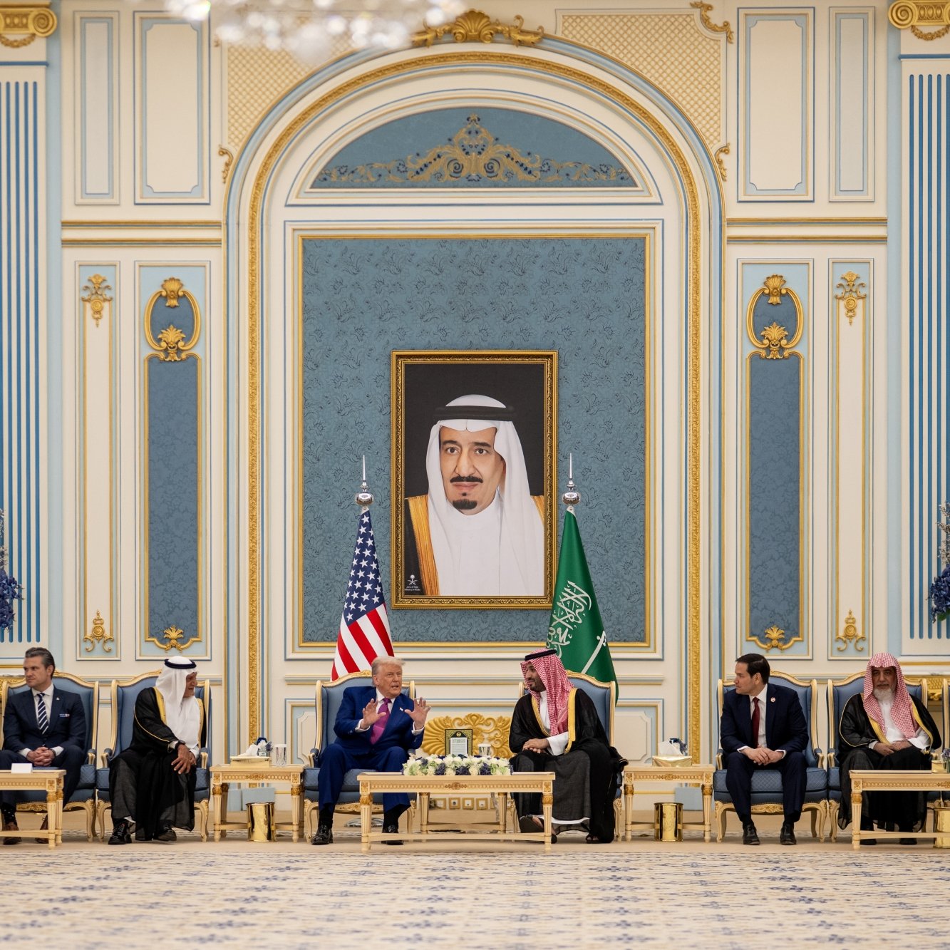 Réunion officielle dans un palais, drapeaux américain et saoudien, hommes en costume autour d'une table.