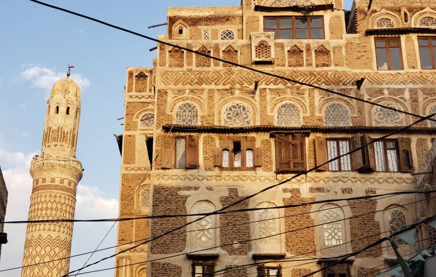 A tall, ornate tower beside a traditional brick building with intricate patterns and wooden windows.